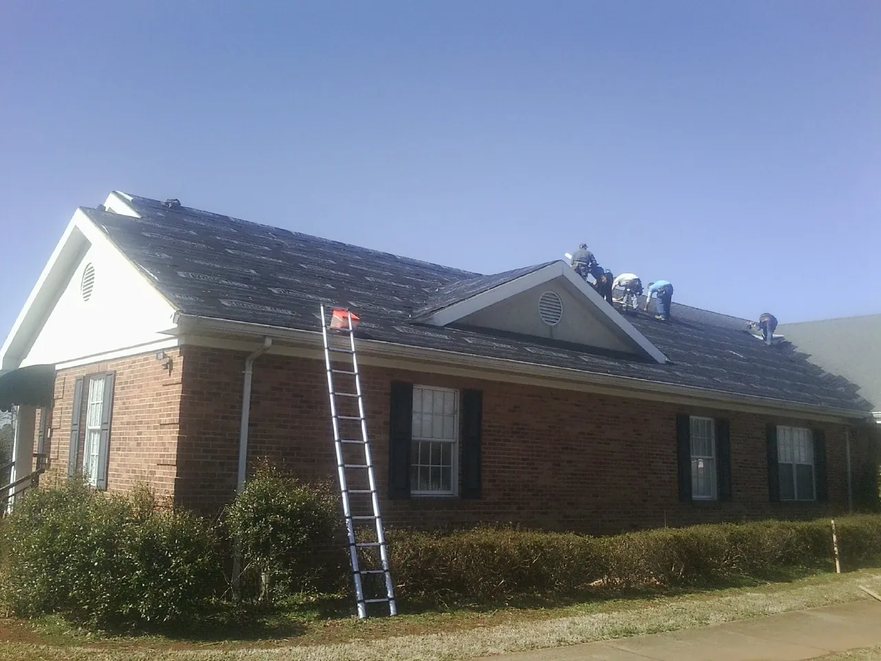 Crew tearing shingles off a brick ranch roof with a ladder set — Emergency Roof Repair work by our crew in Wahoo