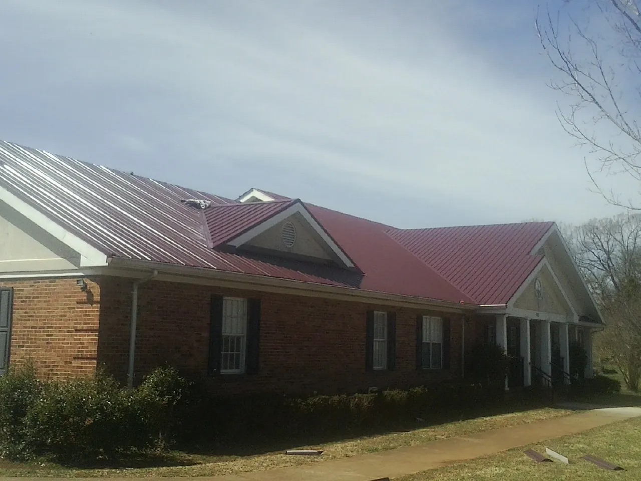 Red metal roof with gabled entries on a long brick building, from a Hail Damage Roof Repair job in Wahoo