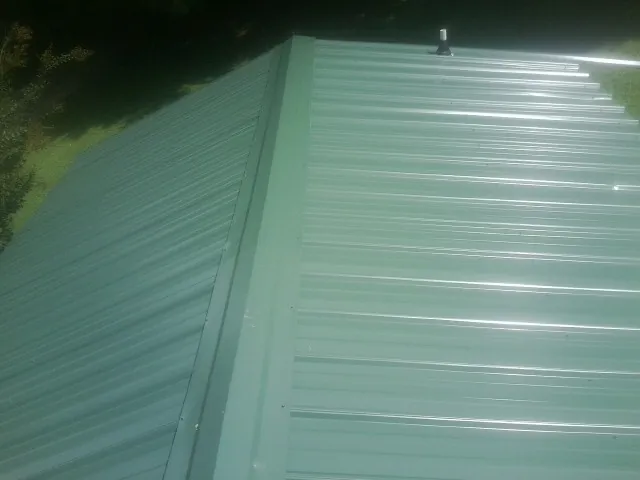New green metal panels meeting at the ridge of a roof — Flat Roof Repair work by our crew in Wahoo