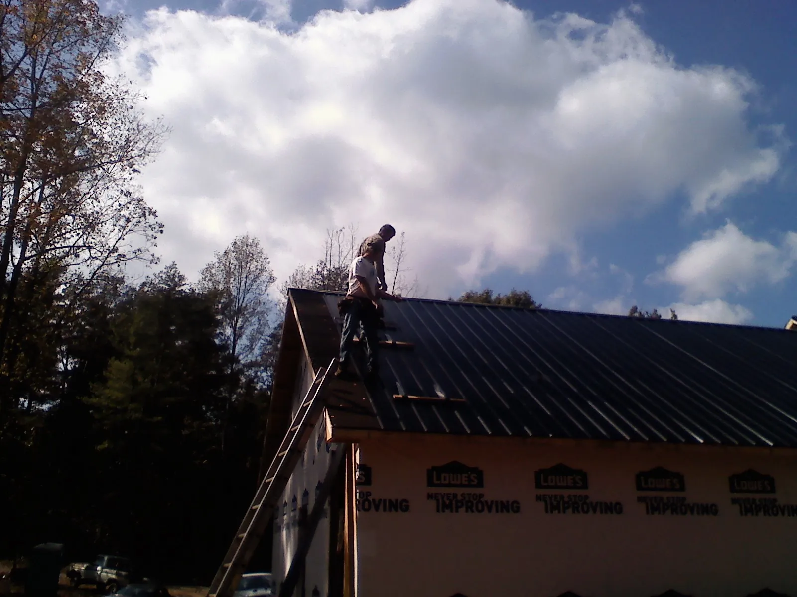 Roofer fastening dark metal panels high against a cloudy sky, from a Roof Inspection job in Wahoo