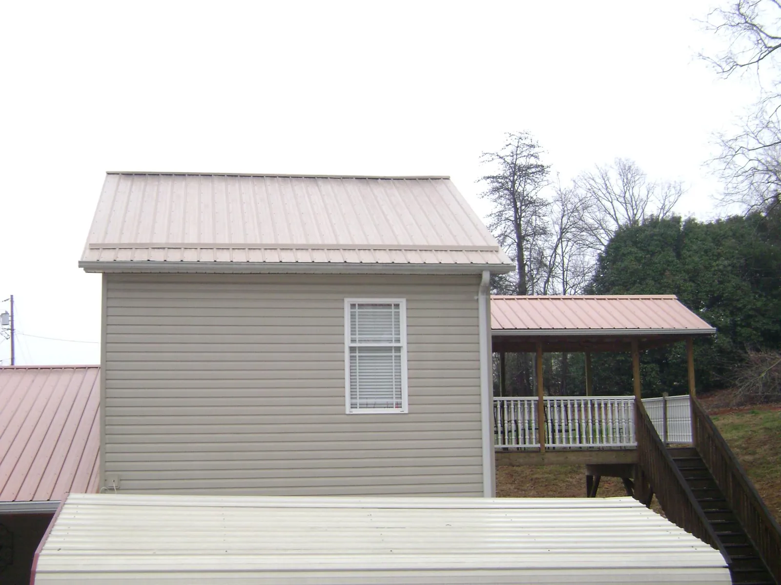 Tan metal roofs on a two story addition and attached porch, from a Roof Replacement job in Wahoo